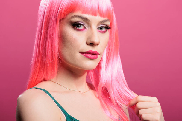 Porträt einer stilvollen Person mit pinkfarbener Perücke, die vor der Kamera posiert und sich im Studio selbstbewusst und unbeschwert fühlt. Attraktive sinnliche Frau mit Glamour-Frisur, die elegante Emotionen zeigt. - Foto, Bild
