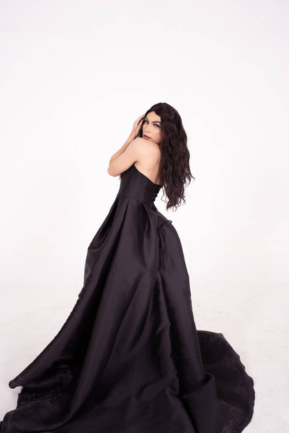 Mulher bonita com cabelo preto encaracolado enquanto vestindo um vestido preto dentro da sala branca - Foto, Imagem