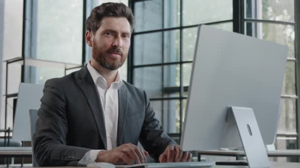 Close-up adult bearded 40s businessman manager office worker boss male company CEO typing on computer working online looking at camera showing ok sign approval gesture agree okay symbol in workplace - Video