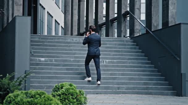 Näkymä takaisin onnistunut liikemies muodollinen puku kävelee portaita moderni toimistorakennus mies ammatillinen johtaja myyntiagentti puhuu puhelimessa vastaamalla liikepuhelu kommunikoida asiakkaan kanssa - Materiaali, video