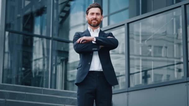 Successful confident caucasian bearded businessman in suit standing outdoors on background office building smiling proud male professional worker leader looking at camera posing with crossed arms - Footage, Video