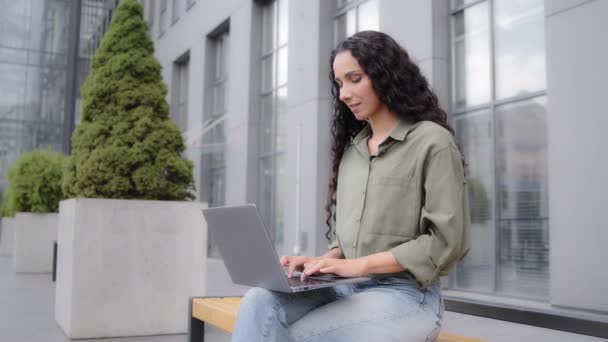 Латиноамериканка 30-летняя предпринимательница-фрилансер, сидящая на открытом воздухе с ноутбуком, работающим в городе, в чате, печатая компьютерный управляющий маркетинговый проект с помощью сетевого веб-сайта - Кадры, видео