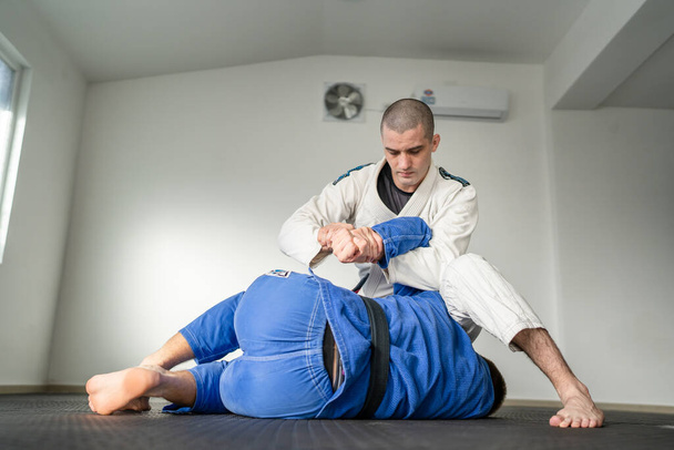 Braziliaanse jiu jitsu bjj training of het sparen van twee atleten vechters dille martial arts techniek in de sportschool op de tatami matten dragen kimono gi zwarte gordel instructeur demonstreren indiening kimura - Foto, afbeelding