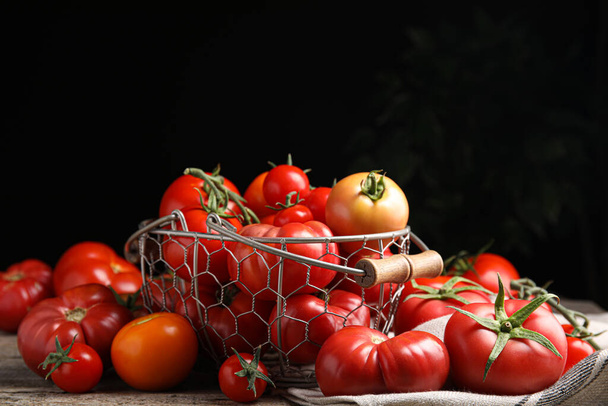 Many different ripe tomatoes on wooden table against dark background - Foto, imagen