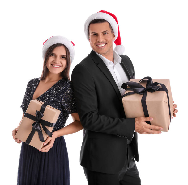 Beautiful happy couple in Santa hats holding Christmas gifts on white background - Zdjęcie, obraz