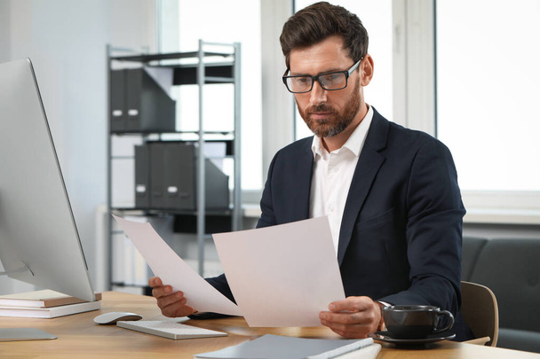 Handsome bearded man working with documents at table in office - Photo, image