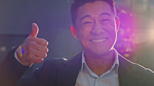 Muotokuva onnellinen hymyilevä hammas tyytyväinen onnistunut iloinen Aasian 40s keski-ikäinen mies pomo liikemies seisoo ulkona auringonvalossa auringonsäteet osoittavat peukalo ylös samaa mieltä hyvän eleen näköinen kamera - Materiaali, video