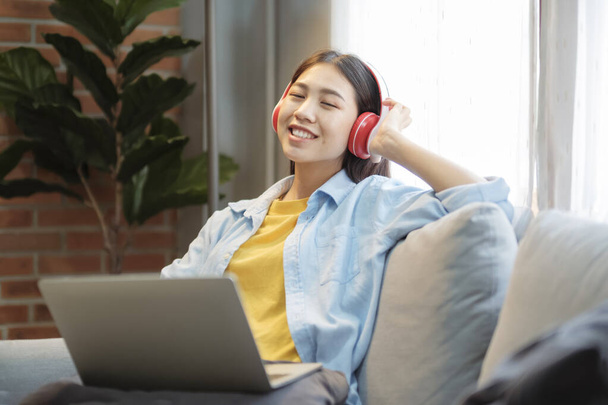 Rest And Relax Concept. Happy woman woman sitting and leaning back on couch at home, listening to music, audio book, podcast, enjoying meditation for sleep and peaceful mind in wireless headphones. - Photo, Image