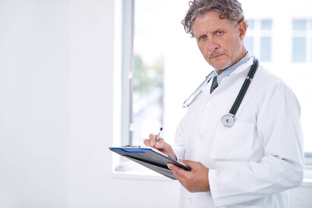 I see your last checkup was five years ago. Portrait of a mature doctor standing in his office and holding a clipboard - Zdjęcie, obraz