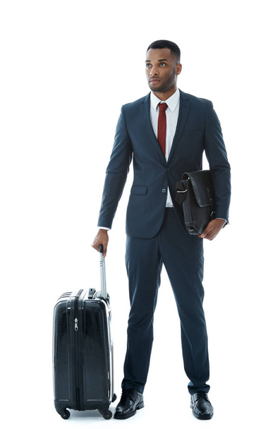Seyahat için hazır. Yakışıklı, genç, Afro-Amerikan bir iş adamı, beyaz bir bavulun yanında duruyor. - Fotoğraf, Görsel