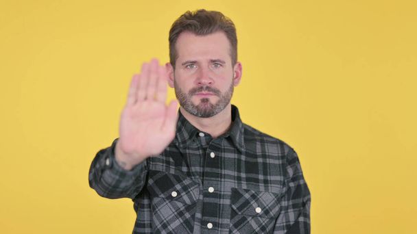 Retrato del hombre adulto maduro mostrando el signo de parada a mano, fondo amarillo - Foto, Imagen