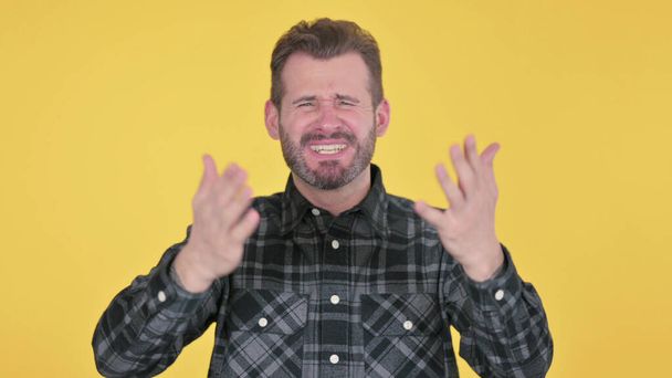 Portret van teleurgestelde volwassen man reageert op verlies, gele achtergrond - Foto, afbeelding