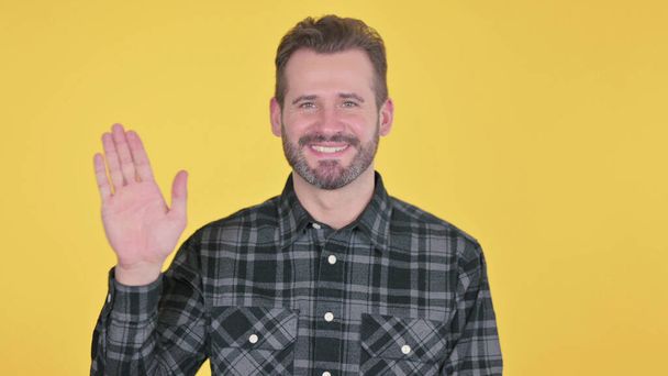 Porträt eines erwachsenen Mannes, der zur Begrüßung winkt, gelber Hintergrund - Foto, Bild