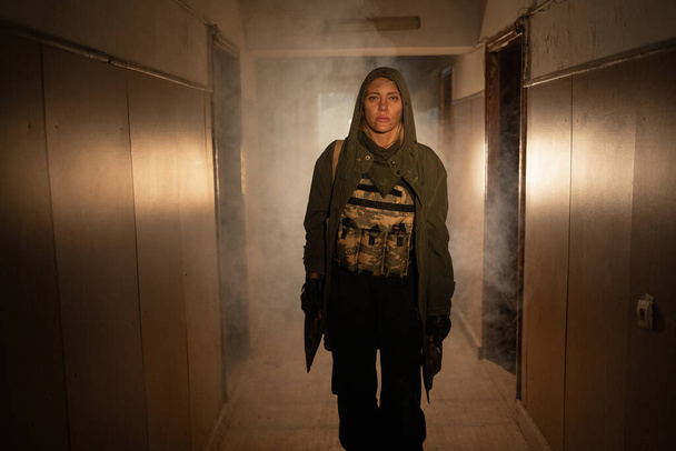 Moedige vrouwelijke soldaat loopt in een vervuild post apocalyptisch verlaten gebouw met smog: milieuramp en apocalyps concept. wijnoogst - Foto, afbeelding