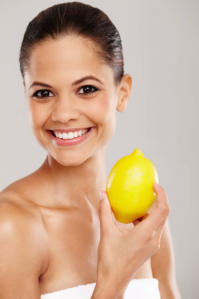 Its my beauty secret. Cropped portrait of a smiling woman holding up a fresh lemon - isolated - Fotografie, Obrázek