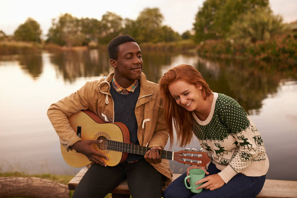 Sabe que la clave de su corazón es la risa. un adolescente serenata a una hermosa chica mientras está sentado junto a un lago - Foto, Imagen