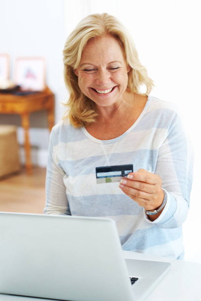 Kommst du vom Himmel? Eine glückliche Seniorin lächelt mit ihrem Laptop über ihre Kreditkarte - Foto, Bild