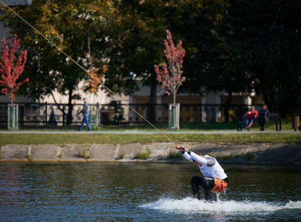 Wakeboarder surfuje nad jeziorem. Młody surfer bawiący się na wakeboardzie w parku kablowym. Sport wodny, koncepcja aktywności na świeżym powietrzu. - Zdjęcie, obraz