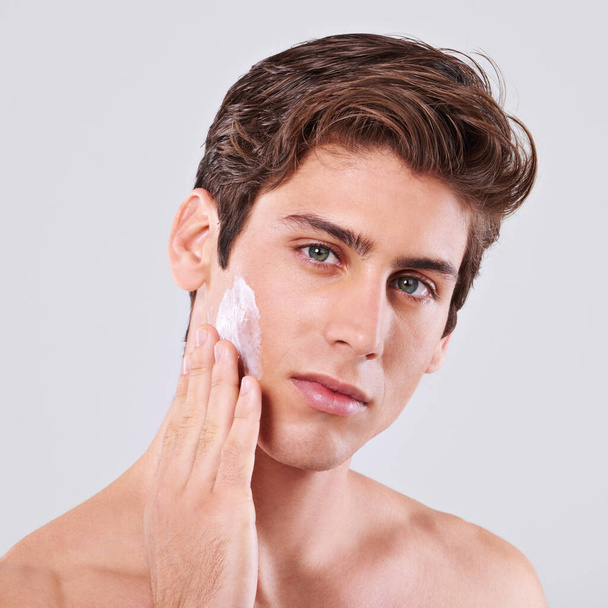 All man and all smooth. Studio shot of a handsome bare chested young man applying lotion to his face - Photo, Image