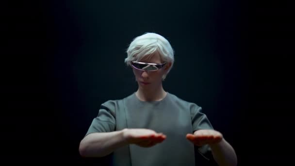 VR elemanı arttırılmış gerçekliği yakından araştırıyor. Futuristik gözlüklerle odaklanmış oyuncu karanlık arka planda metaevren simülasyonu yaşıyor. Siber sanal nesnelere ışık tutan şık sarışın adam.. - Video, Çekim