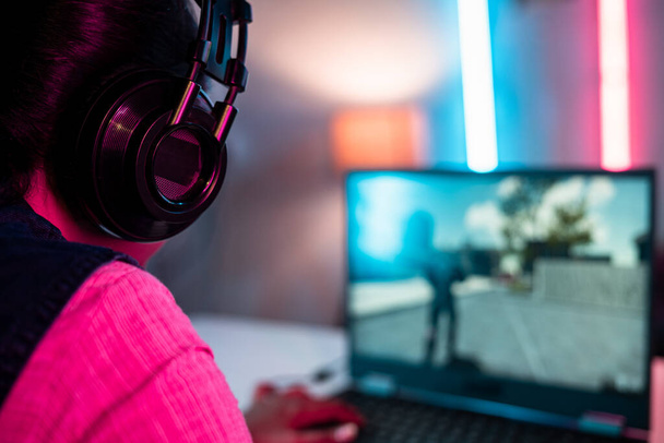 Back view close up shot of gamer with headphones playing online video game on laptop at home - concept of competition, tournament and entertainment. - 写真・画像