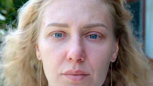 Portrait of a tired sick woman with blue eyes looking at the camera. The woman has reddened eyelids and wet eyes. Girl looks tired and sad, going through grief. - Footage, Video