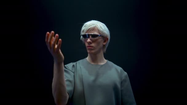 Futuristic man experiencing virtual reality closeup. Cyber teenager gesturing select simulation objects in dark background. Focused gamer immersing metaverse in hi tech glasses. Future reality concept - Footage, Video