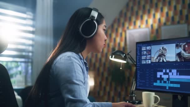Asiatin im Headset bearbeitet Video mit Astronauten für Client im Programm am PC, während sie vom Home Office aus am Tisch arbeitet. Freiberufliche Tätigkeit - Filmmaterial, Video