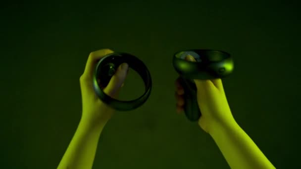 Anonieme speler gebruikt joysticks in futuristische augmented reality close-up. Onbekende persoon controllers ervaren vr simulatie in de donkere kamer. Multi gekleurde menselijke armen gebaar selecteert objecten neon licht - Video