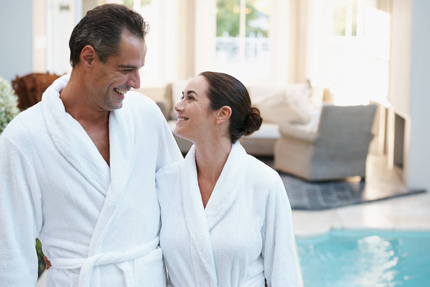 Sharing a loving glance after an afternoon swim. a couple in robes beside a pool - Photo, image