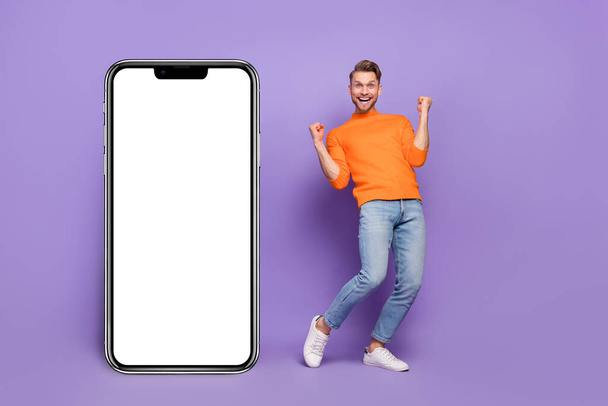 Full body photo of laughing screaming man excited to win new phone model isolated on purple color background. - Photo, image