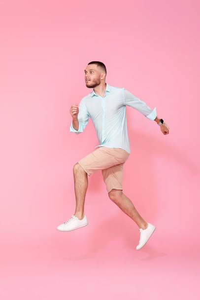 surprised young man in summer clothes jumping isolated on pink background. Full length - Foto, Imagem
