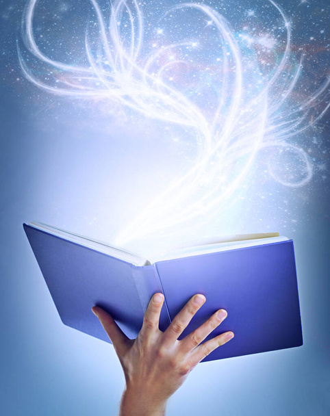 Lassen Sie sich in magische neue Welten ziehen. eine Hand hält ein geöffnetes Bilderbuch mit Licht, das von ihm ausgeht - Foto, Bild