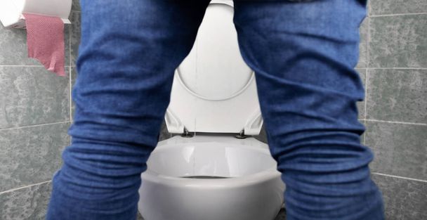 Prostatitis-Konzept. Rückansicht eines Mannes, schwer zu pinkeln. Schwierigkeiten beim Wasserlassen mit Prostatitis. Blick auf die Toilette und die Beine eines Mannes. Imitation von Urin mit klarem Wasser. Krank auf der Toilette - Foto, Bild