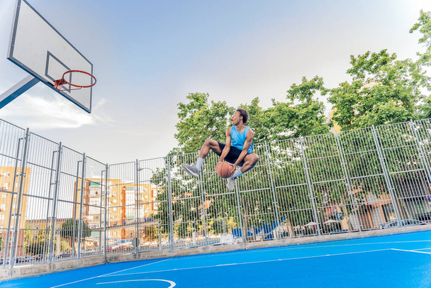 Unrecognized african boy wearing sports clothes playing basketball and throwing the ball. - Photo, image