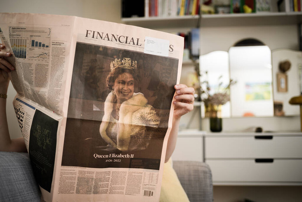 Париж, Франция - 9 сентября 2022 года: Женщина читает на диване в гостиной последнюю страницу газеты Financial Times, отдавая дань уважения королеве после ее смерти - Королева Елизавета II умерла в замке Балморал - Фото, изображение