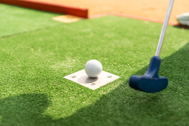 A club prepares to hit a ball during a mini golf game. - Φωτογραφία, εικόνα