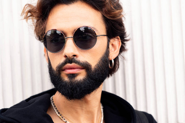 close up portrait of a beautiful young man with beard and sunglasses in a white background, concept of urban lifestyle and stylish clothing - Foto, afbeelding