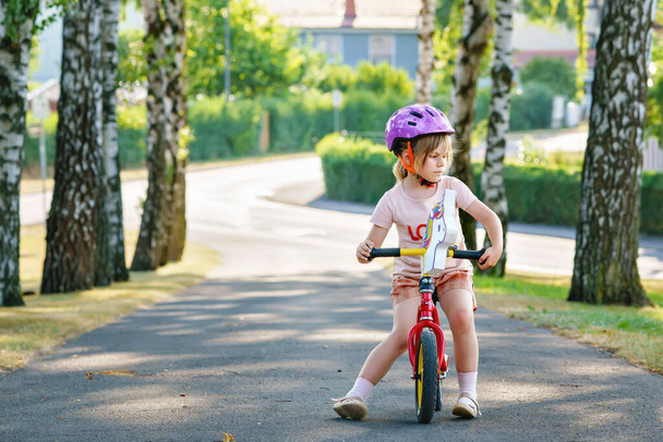 Yaz günü kasklı, denge bisikletiyle koşan küçük anaokulu kızı. Mutlu çocuk sürüşü, bisikletle bisiklet sürme, açık hava aktiviteleri. Mutluluk, çocukluk. Çocuklar için yaz etkinliği - Fotoğraf, Görsel