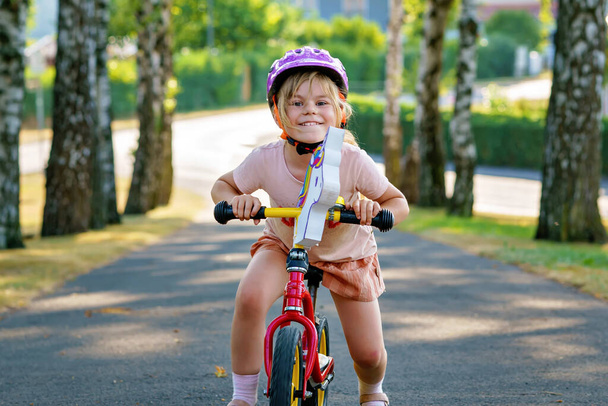 Little preschool girl with helmet running with balance bike on summer day. Happy child driving, biking with bicycle, outdoor activity. Happiness, childhood. Summer activity for children - Photo, Image