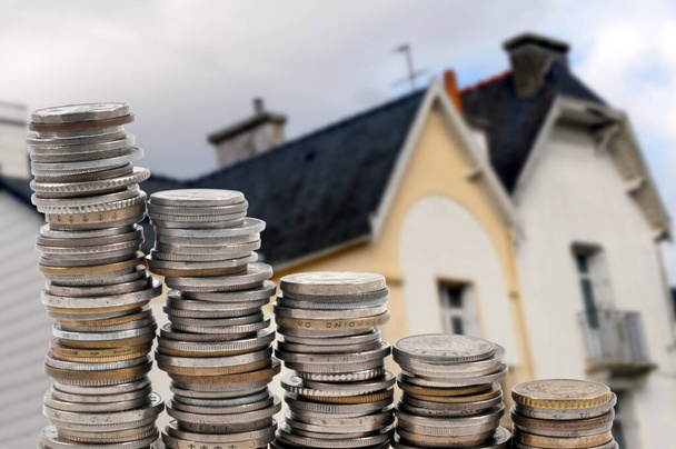 Concepto de inversión inmobiliaria con pilas de monedas y una casa borrosa en el fondo  - Foto, imagen