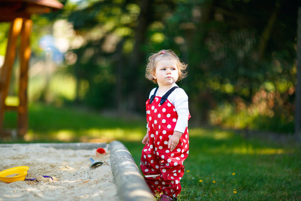 Dışarıda parkta kumlarda oynayan tatlı bir kız çocuğu. Kırmızı sakız pantolonlu güzel bebek güneşli yaz gününde eğleniyor. Renkli kum oyuncakları olan çocuk. Sağlıklı aktif bebek dışarıda oyunlar oynuyor. - Fotoğraf, Görsel