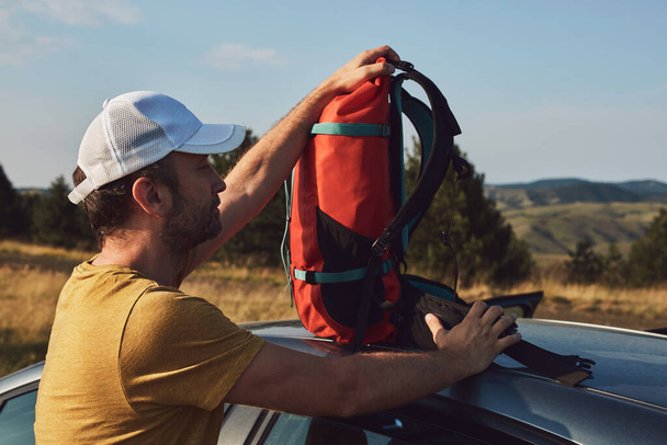 Man camping and hiking in nature, unpacking from car outdoors, recreation and hobbies. - Photo, Image