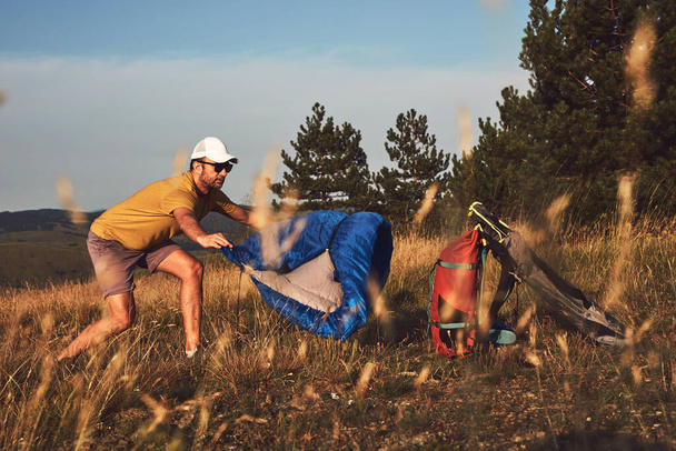 Mężczyzna kemping w przyrodzie, rozpakowywanie i pakowanie małych namiotów na zewnątrz, rekreacji i hobby. - Zdjęcie, obraz