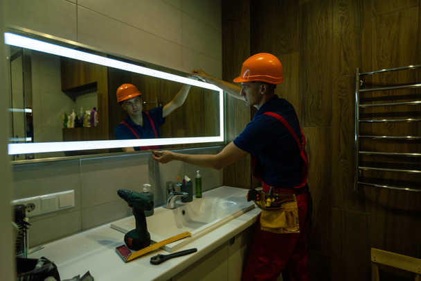 Male repairman hangs the modern electronic bathroom mirror. accessories and furniture for bathrooms and houses. - Foto, imagen