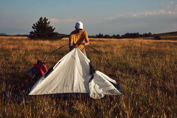 Férfi kemping a természetben, kicsomagolás és csomagolás kis sátor szabadban, kikapcsolódás és hobbik. - Fotó, kép