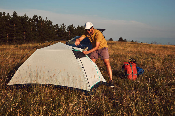 Man camping in nature, unpacking and packing small tent outdoors, recreation and hobbies. - 写真・画像