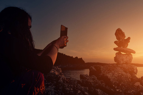 Силует жінки, що балансує скелі та камені на узбережжі океану на заході сонця
. - Фото, зображення