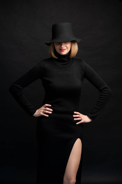 schöne junge Frau in schwarzem Kleid und Hut auf dunklem Hintergrund - Foto, Bild