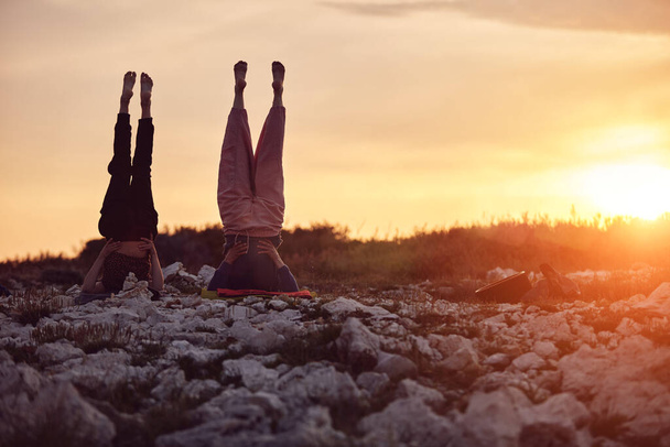 Mutter und Tochter praktizieren gemeinsam Yoga in der Natur bei Sonnenaufgang. - Foto, Bild